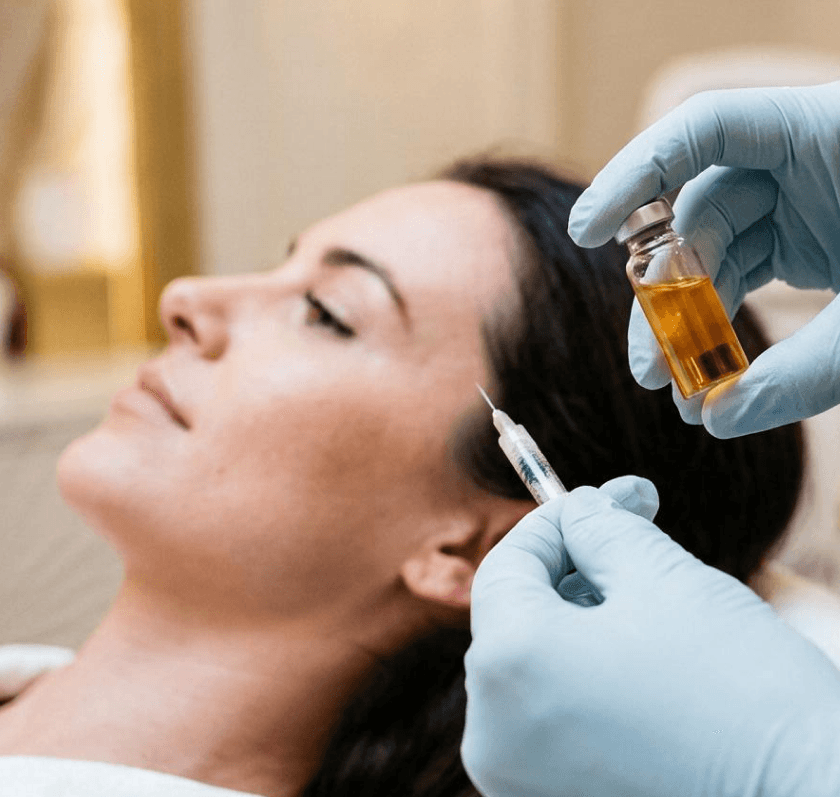 A clinician in blue gloves preparing a PRP injection near a reclined patient's hairline