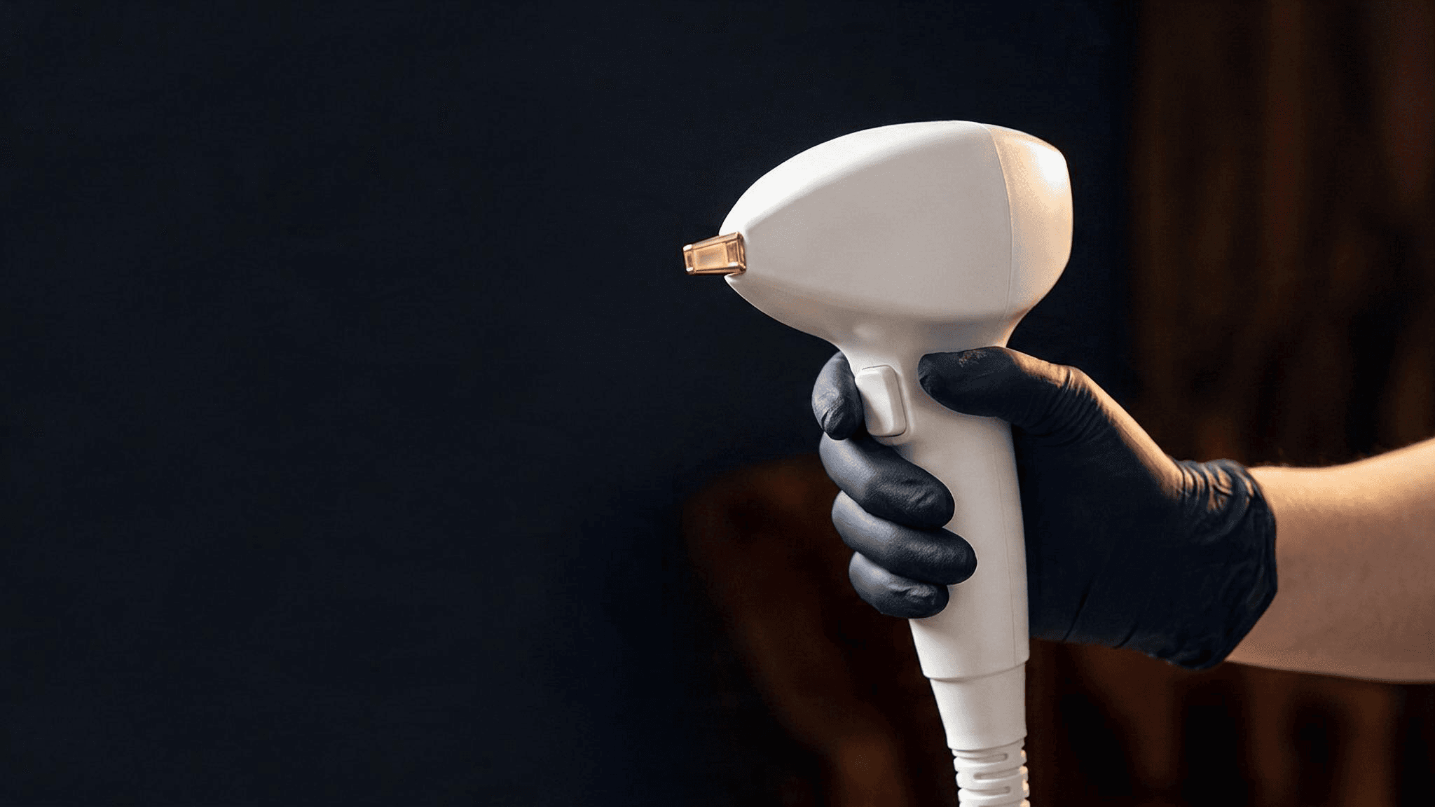 A gloved hand holding the Vasculaze handpiece against a dark studio backdrop