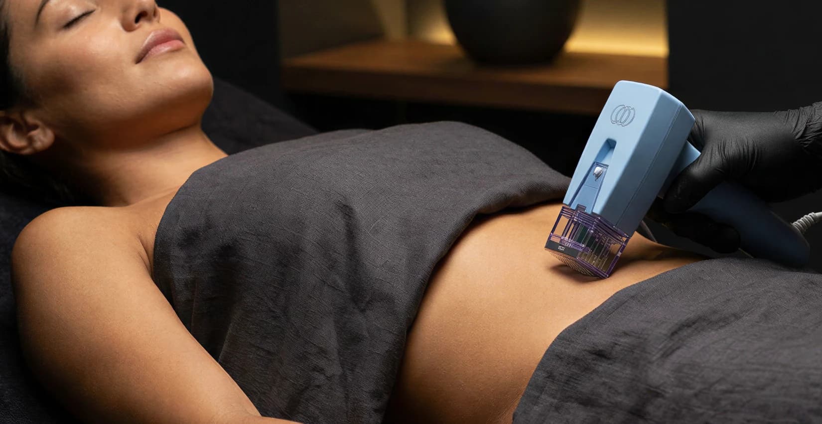 A patient receiving a body contouring treatment with a handheld device on the abdomen