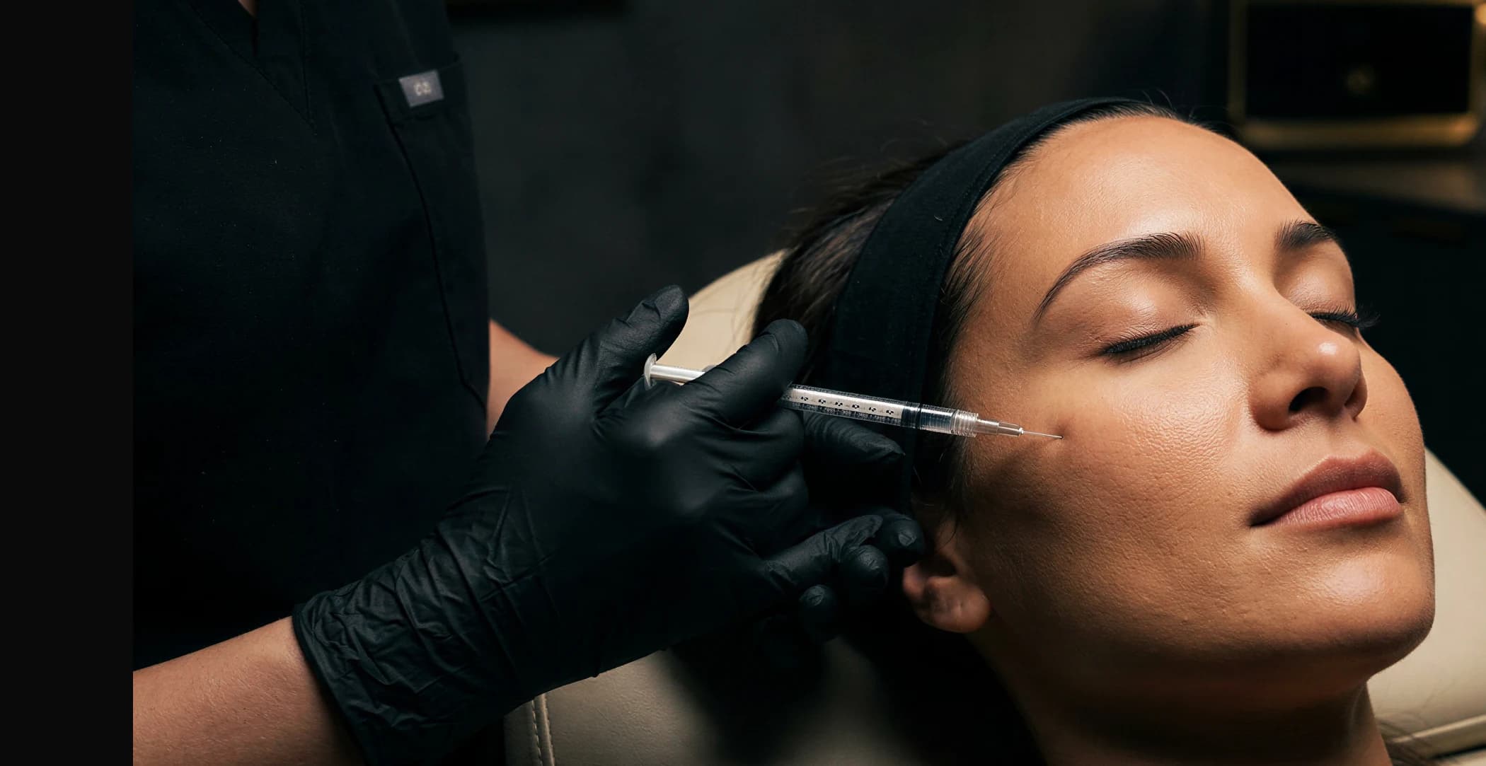 A patient receiving a Botox injection near the brow in a dimly lit treatment room