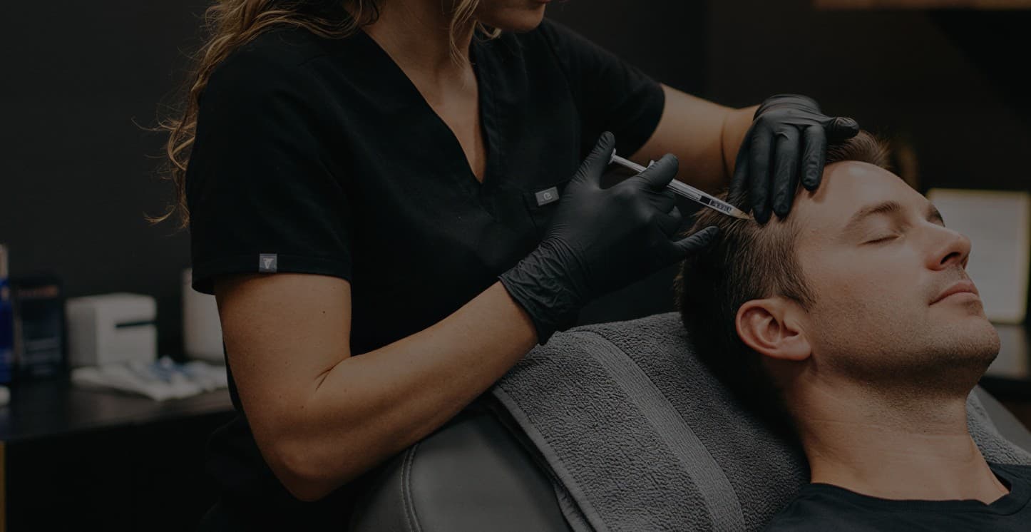 A clinician applying a scalp treatment device to a reclined male patient's hairline