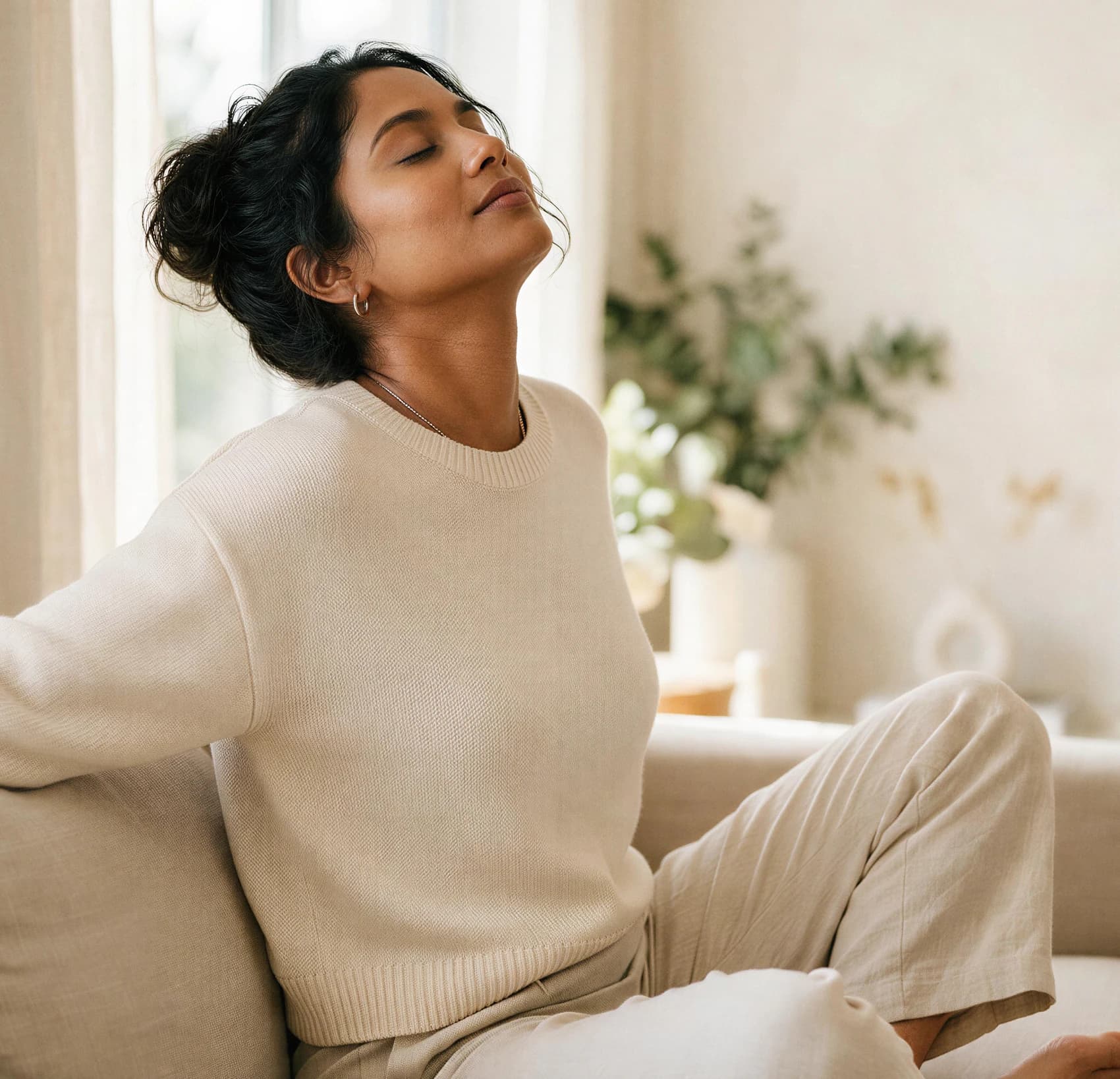 A relaxed woman in a cream sweater stretching on a sofa in soft daylight