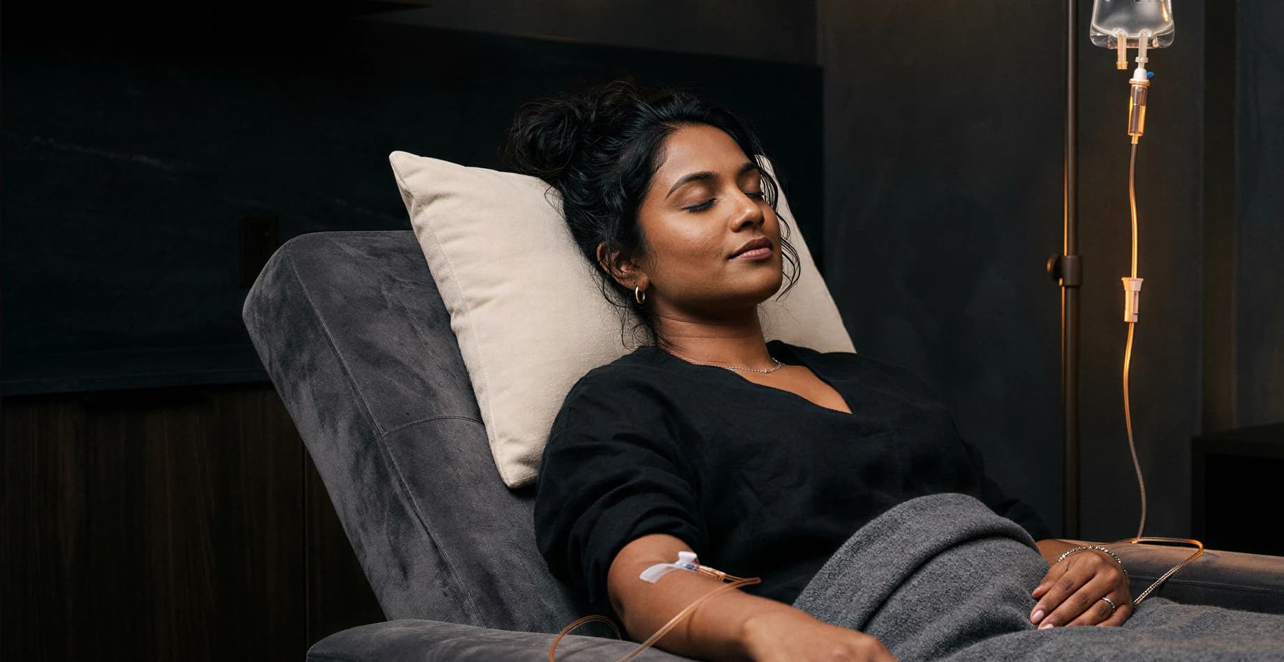 A patient reclining in a dim luxury lounge while receiving an IV infusion