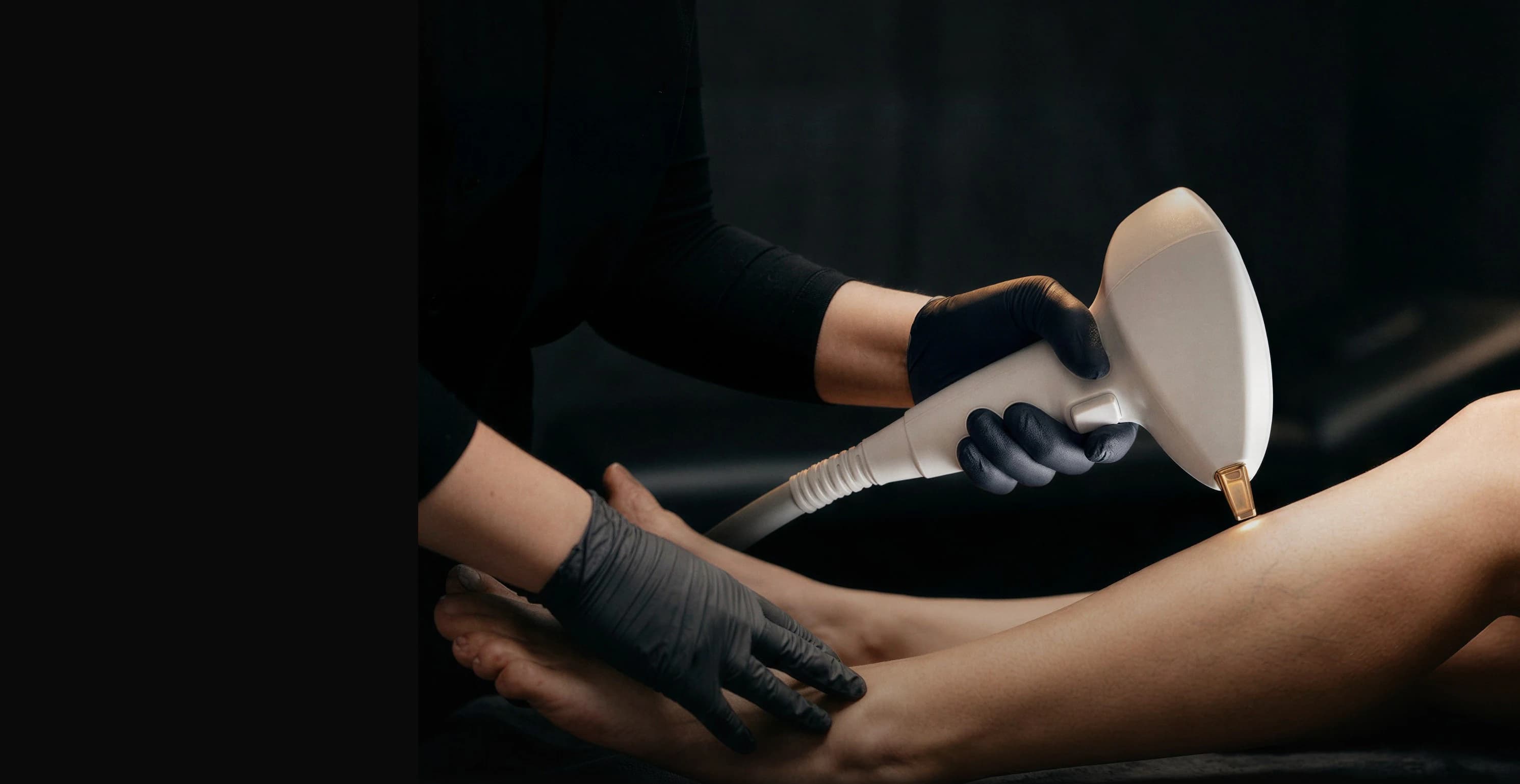A practitioner in black gloves treating a patient's leg with a handheld vascular laser device