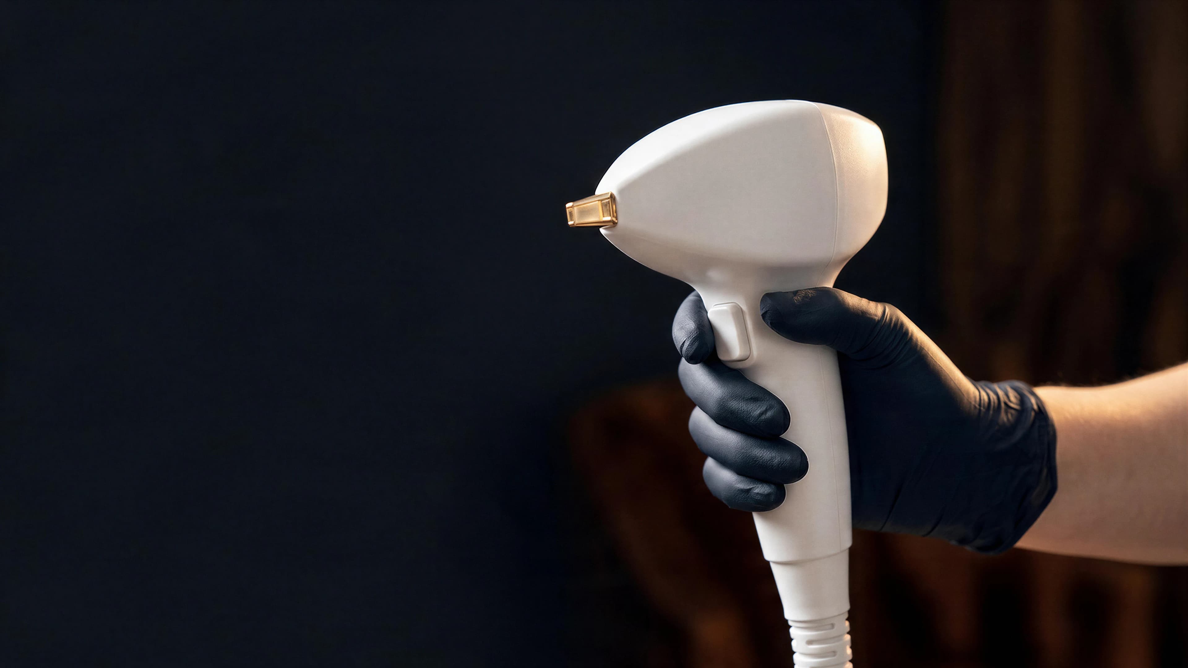 A gloved hand holding the Vasculaze handpiece against a dark studio backdrop